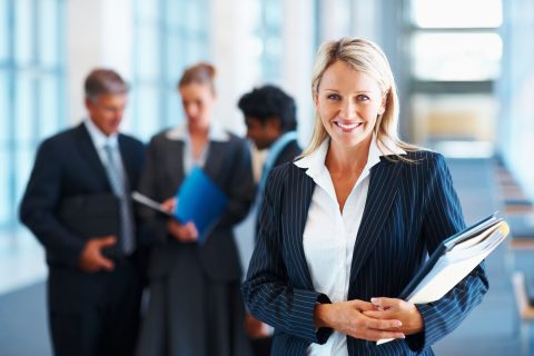 Lächelnde Frau im Business Dress vor einer kleinen Gruppe Kolleginnen und Kollegen