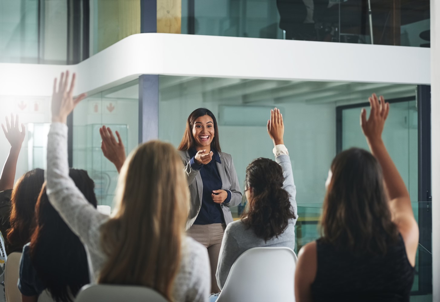 Blick aus den hinteren Reihen eines Publikums auf eine junge Moderatorin bei einer Veranstaltung. Die jungen Frauen im Publikum haben die Hände. - XXtalents - die Jobbörse für Frauen